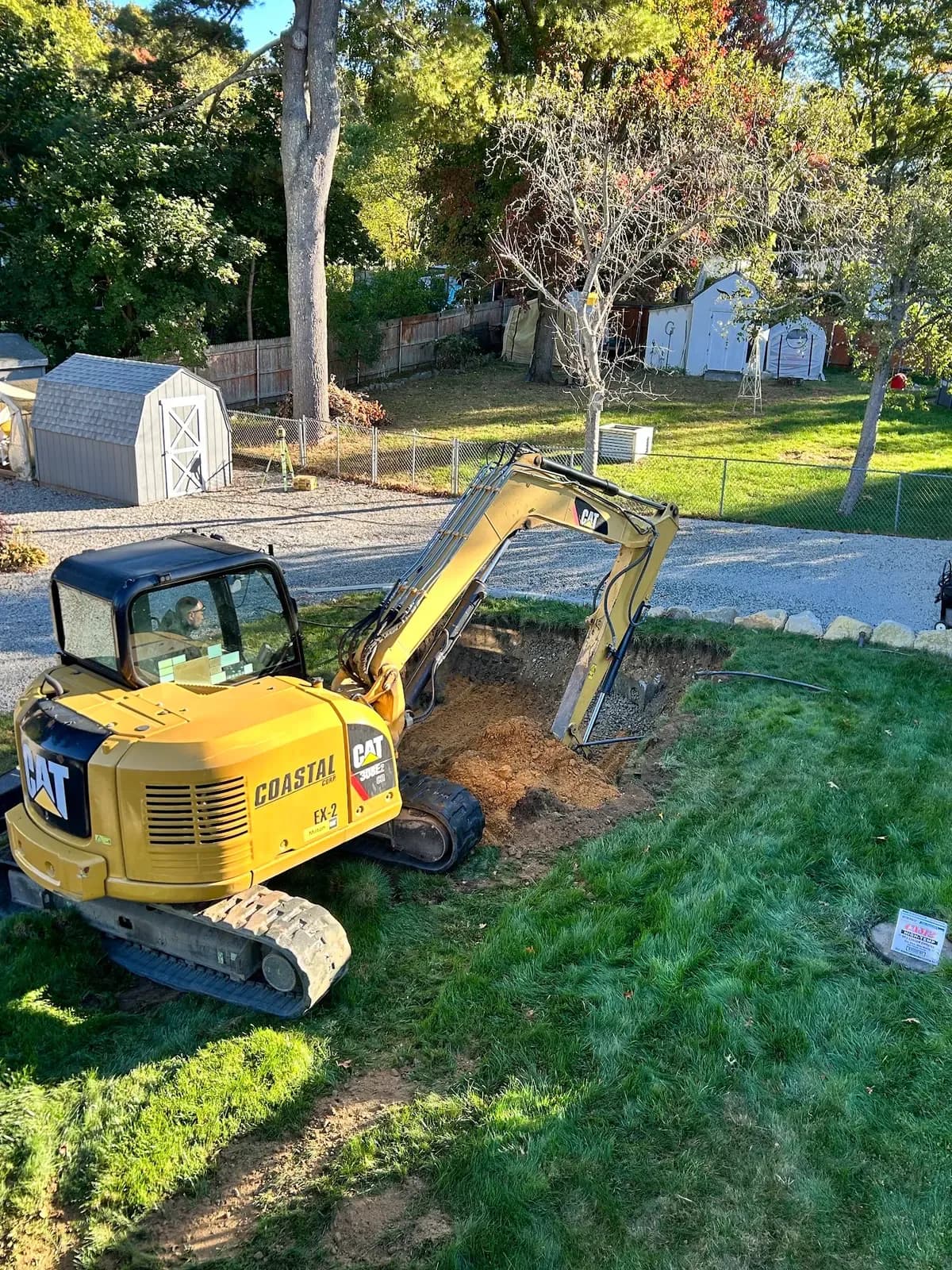 A Coastal Corp CAT 308 excavator digs a foundation excavation in a residential yard.