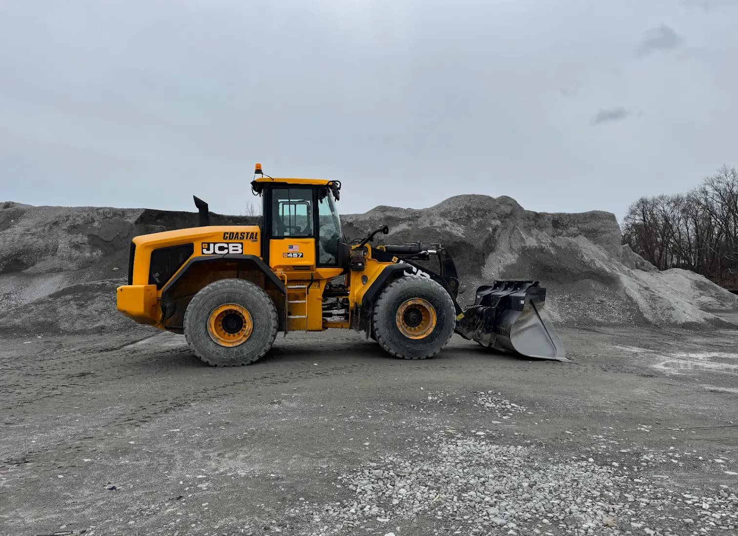 A Coastal Corp JCB 457 wheel loader staged in front of large material stockpiles at the yard.